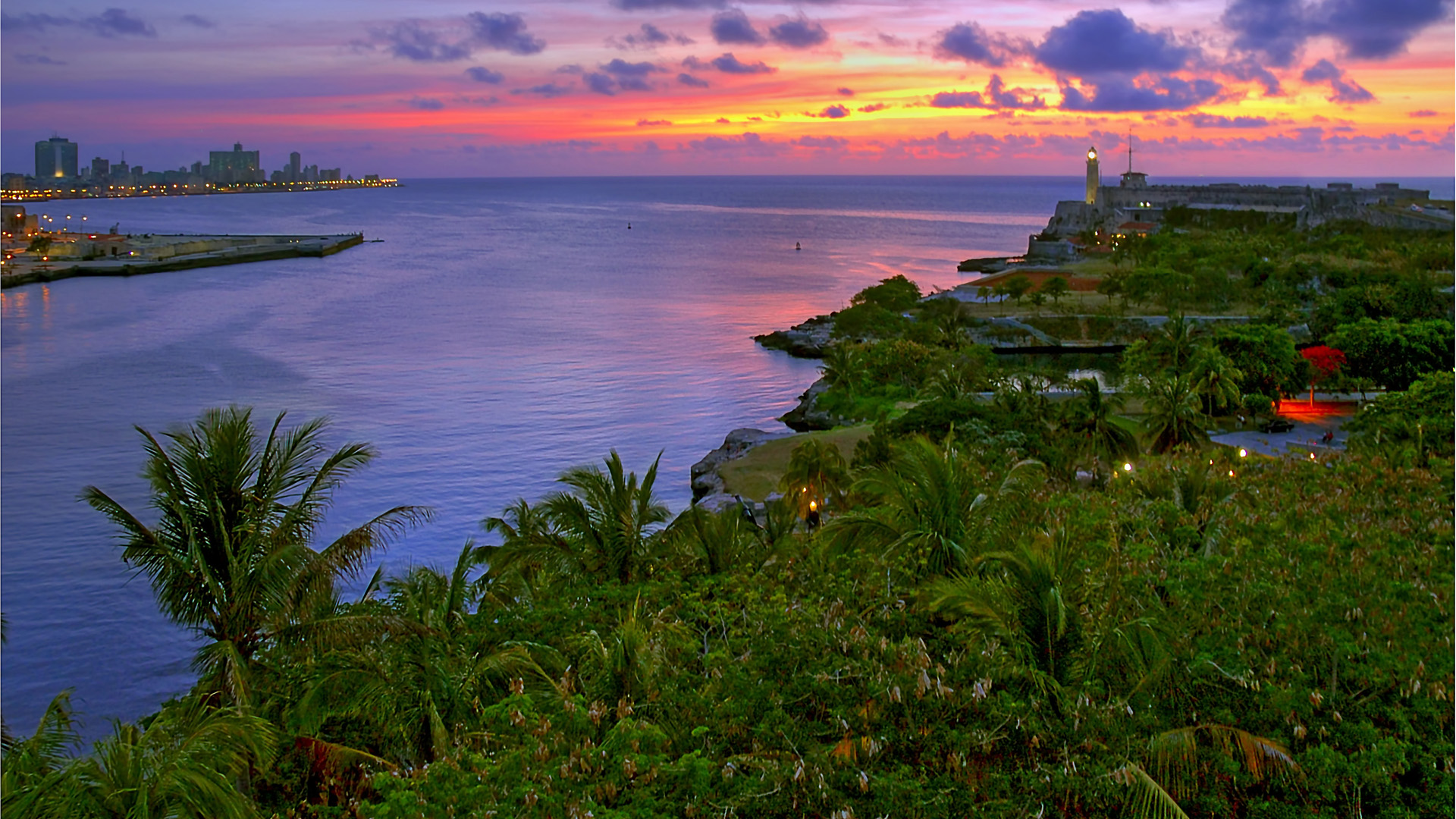 Cuba. Morro Castle and entrance to Havana Bay, seen from the La Cabaña at dusk. Beautiful tropical garden in the foreground.