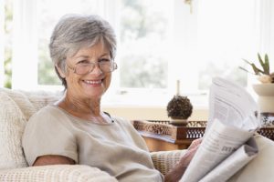 Woman in living room reading newspaper smiling