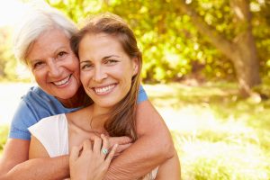 Senior woman sitting outdoors with her adult daughter, smiling to camera